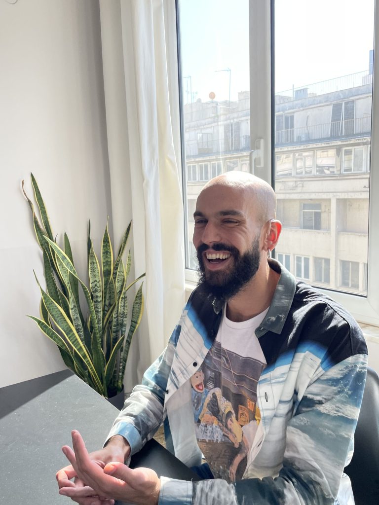 A portrait of Sergio smiling warmly while sitting in an office near a window and houseplant.
